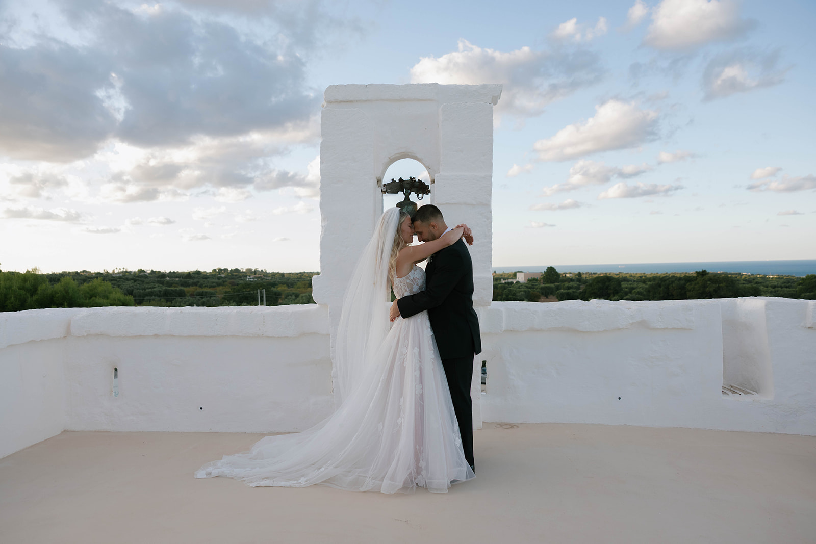 The newlyweds beneath the rooftop bell with the sea beyond